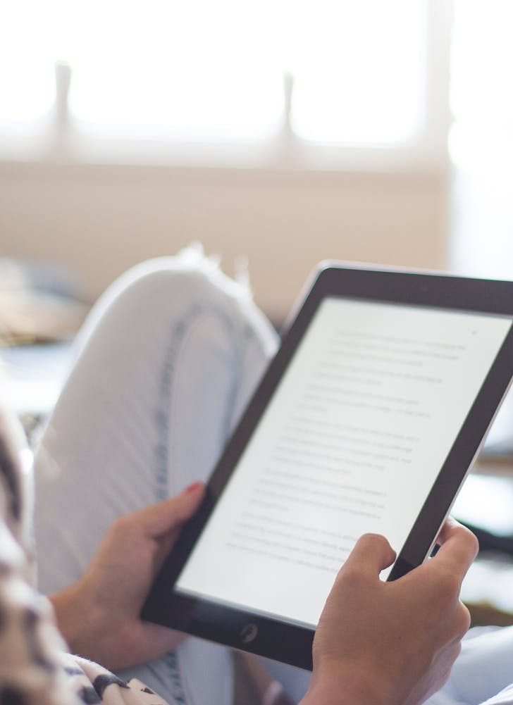 A woman enjoys reading on a tablet, sitting comfortably in a modern living room.